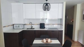 Eine kompakte Küche mit weißen Schränken, einer eingebauten Mikrowelle, einer Kaffeemaschine und einem Essbereich mit Tisch und Stühlen.