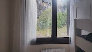 Ein Zimmer mit Fensterblick auf eine felsige Klippe und viel Grün, inklusive Heizkörper und einem Stockbett.