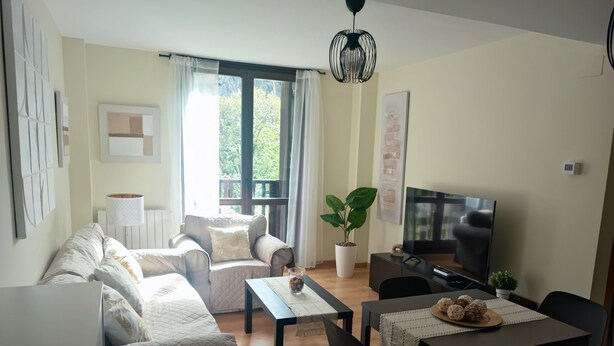 Ein Wohnzimmer mit einer Couch, einem Couchtisch, einem Fernseher und einem Esstisch mit Stühlen.