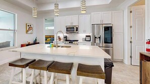 A modern kitchen with white cabinets, stainless steel appliances, and a central island with bar stools. - Dog-friendly Waterfront home with private pool, on-site fishing (Cape Coral)