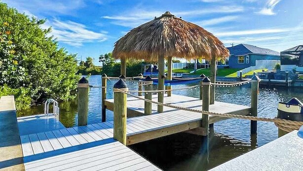 A wooden dock with a thatched-roof gazebo, a water body, and houses in the background. - Dog-friendly Waterfront home with private pool, on-site fishing (Cape Coral)