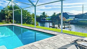 A swimming pool with a glass enclosure, a dock, and a view of a water body. - Dog-friendly Waterfront home with private pool, on-site fishing (Cape Coral)
