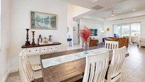 A dining area with a wooden table, white chairs, a vase with red flowers, and a painting on the wall. - Dog-friendly Waterfront home with private pool, on-site fishing (Cape Coral)
