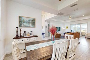 A dining area with a wooden table, white chairs, a vase with red flowers, and a painting on the wall. - Dog-friendly Waterfront home with private pool, on-site fishing (Cape Coral)