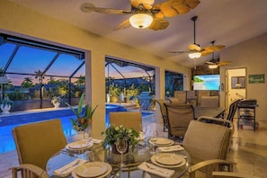 A dining area with a pool view, ceiling fans, and a beach-themed sign. - Canal front home with private pool, direct gulf access, and internet (Cape Coral)