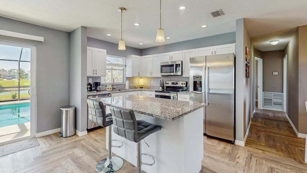 A modern kitchen with a central island, stainless steel appliances, and a view of a swimming pool. - Dog friendly house with private pool, lanai, and washer & dryer (Rotonda West)