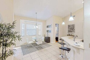 A modern kitchen with a dining area, bar stools, and a large window with blinds. - Canal-front home with pool, outdoor kitchen, & private dock - dog-friendly (Cape Coral)