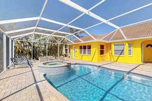 A covered swimming pool with lounge chairs, a hot tub, and a yellow building with a tiled roof. - Waterfront Hideaway | Pool & Private Dock (Cape Coral)