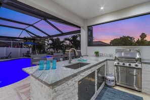A modern kitchen with a built-in gas stove, a sink, and a poolside bar area. - Luxury canal front home with heated pool, pool spa, grill, fireplace, W/D, & AC (Cape Coral)