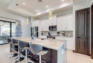 A modern kitchen with white cabinets, stainless steel appliances, and a central island with bar stools. - Luxury canal front home with heated pool, pool spa, grill, fireplace, W/D, & AC (Cape Coral)