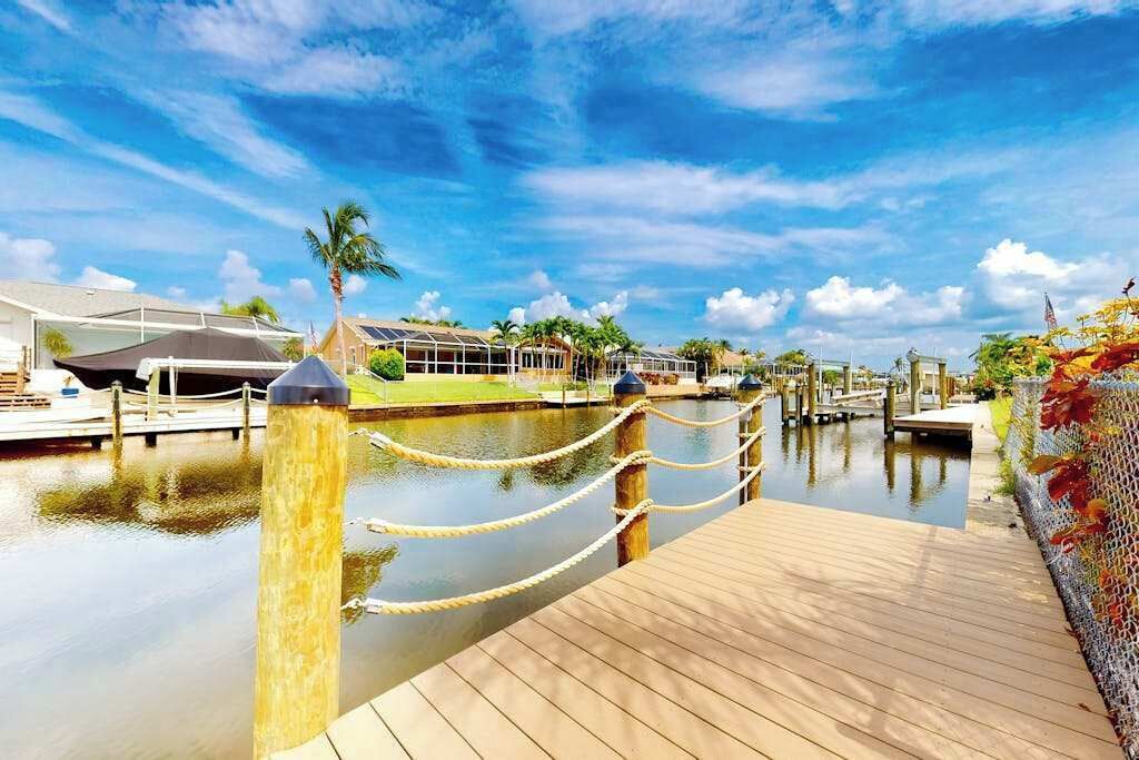 A wooden dock leading to a marina with boats, a clear sky, and a palm tree.