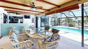 Un'area relax esterna coperta con mobili in vimini, una ventola a soffitto e vista su una piscina.