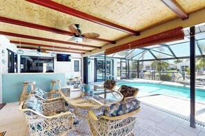 A covered outdoor seating area with wicker furniture, a ceiling fan, and a view of a swimming pool. - Coastal Cabana - canal-front home with private heated pool, dock, inviting patio (Cape Coral)