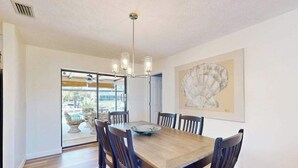 Una sala da pranzo con un tavolo in legno, sei sedie, un lampadario e un grande quadro astratto appeso alla parete.