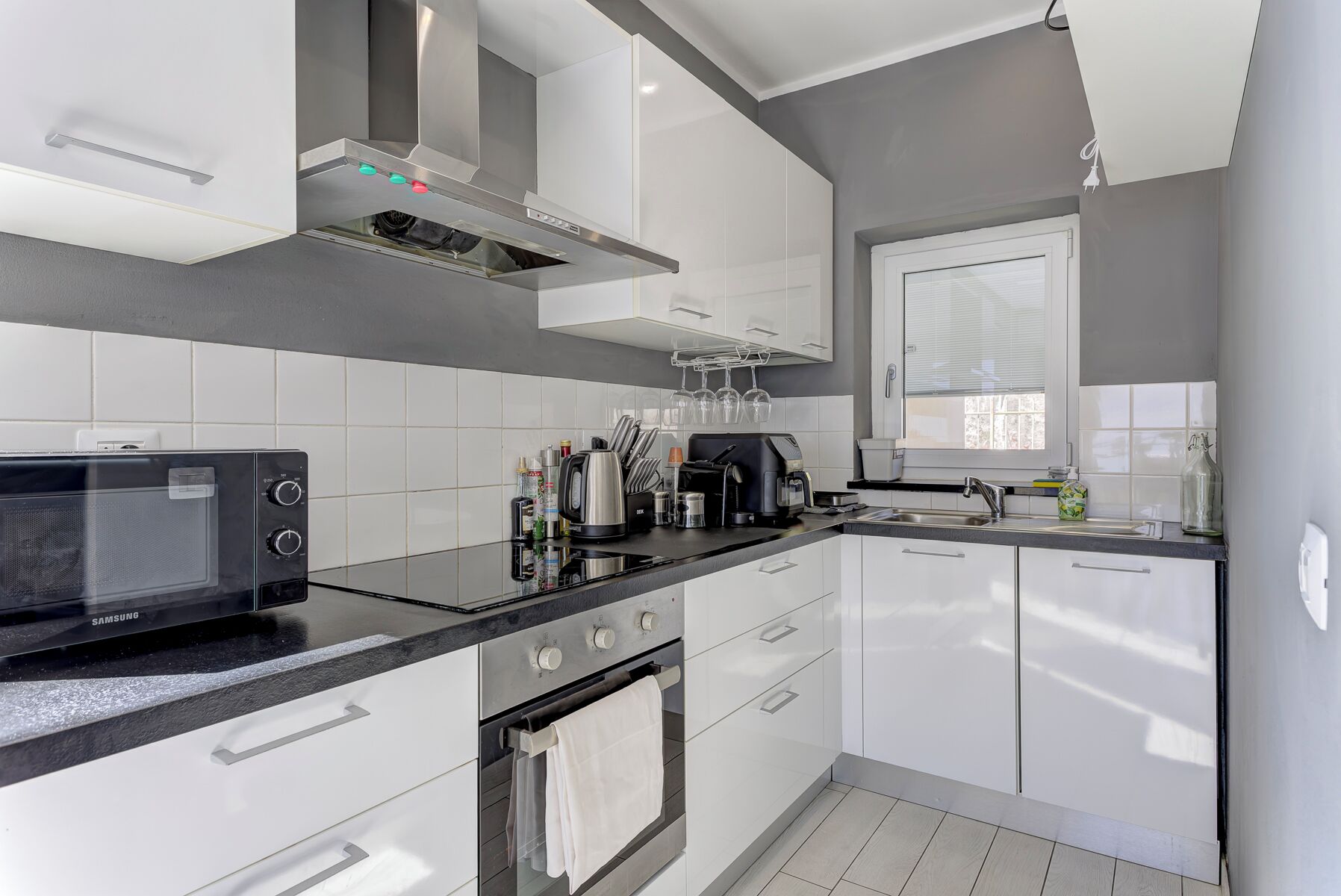 A modern kitchen with a microwave, oven, coffee maker, and a window with blinds.