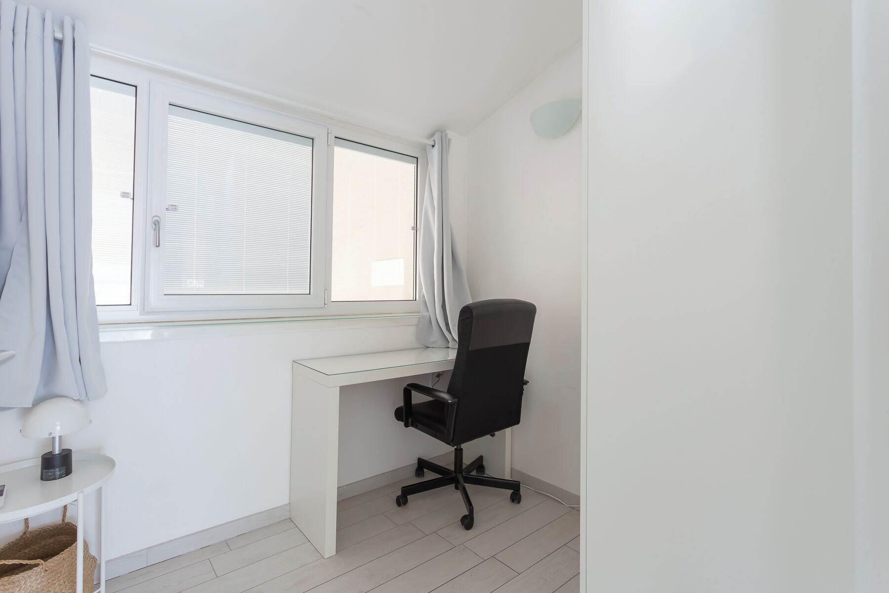 Une pièce comprenant un bureau, une chaise, une lampe et une fenêtre avec des stores.