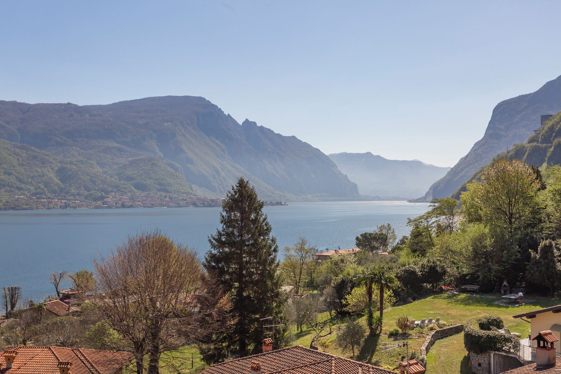 A mountainous landscape with a lake, a small village, and a house with a tiled roof and garden.