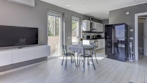 Een moderne keuken met een grote koelkast, een eethoek met een tafel en stoelen, en een flatscreen televisie aan de muur.