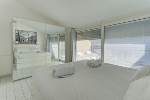A modern hotel room with a large bed, a glass partition, and a view of the city. - Open View Apartment by Wonderful Italy (Onno)