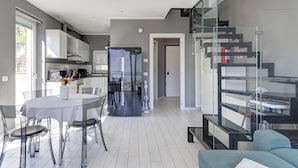 Een moderne keuken met witte kasten, een eethoek met een glazen tafel en stoelen, en een trap met glazen balustrades.