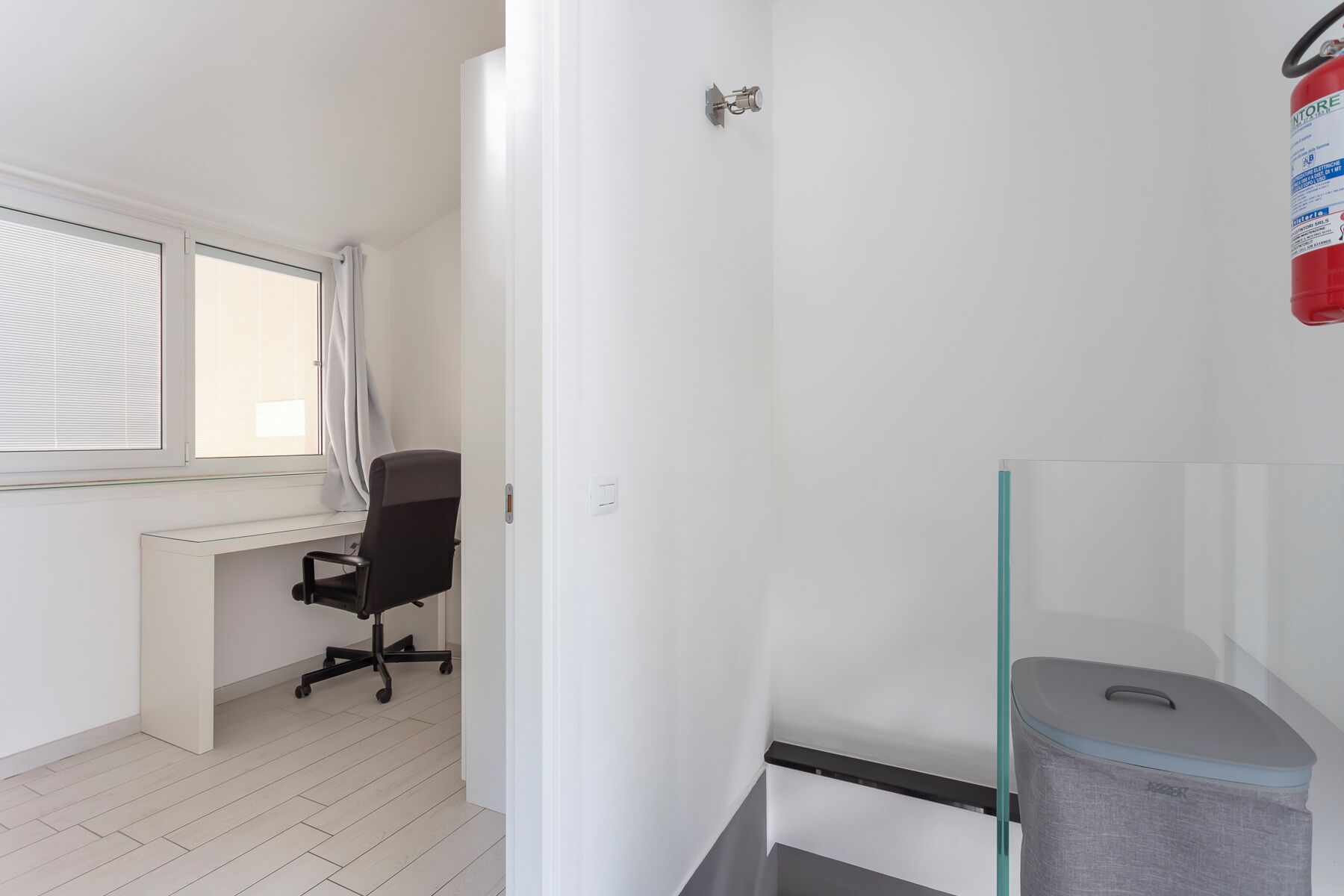 A room with a desk, chair, window, and a trash bin.