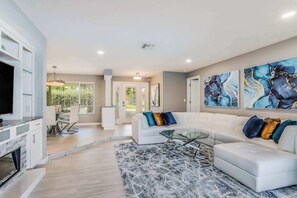 A modern living room with a white sectional sofa, a glass coffee table, and abstract art on the wall. - Waterfront escape in the heart of the action with pool, spa, grill, & WiFi (Cape Coral)