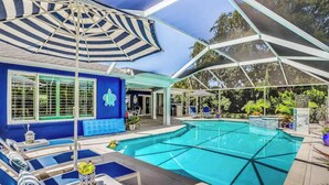 A pool area with lounge chairs, a covered seating area, and a building with a blue exterior.