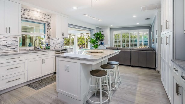A modern kitchen with white cabinets, a central island with stools, and a view of the outdoors through large windows.