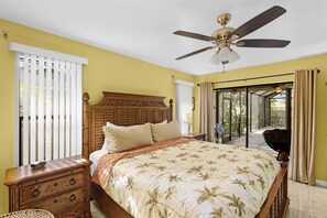 A bedroom with a bed, a nightstand, a dresser, a ceiling fan, and a view through a glass door to an outdoor area. - Cape Escape - Dog-Friendly | Pool, Bar & Fenced Yard (Cape Coral)
