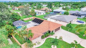 A residential area with houses, a swimming pool, and a solar panel on a roof. - Dog-friendly home with a private heated pool, screened lanai, W/D, & AC (Cape Coral)