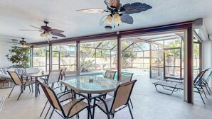 A sunlit patio with a glass-enclosed dining area, ceiling fans, and a view of a swimming pool. - Dog-friendly home with a private heated pool, screened lanai, W/D, & AC (Cape Coral)