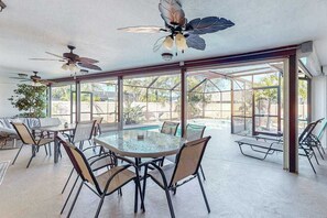 Eine sonnendurchflutete Terrasse mit einem verglasten Essbereich, Deckenventilatoren und Blick auf einen Swimmingpool.