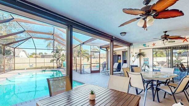 A poolside area with a glass table, chairs, and ceiling fans. - Dog-friendly home with a private heated pool, screened lanai, W/D, & AC (Cape Coral)