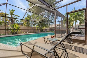 An indoor pool area with a glass enclosure, lounge chairs, and a table with drinks. - Cape Escape - Dog-Friendly | Pool, Bar & Fenced Yard (Cape Coral)