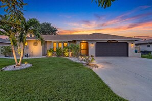 A residential house with a driveway, a well-maintained lawn, and a sunset sky. - Cape Escape - Dog-Friendly | Pool, Bar & Fenced Yard (Cape Coral)