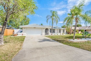 A single-story house with a garage, a front lawn, and palm trees. - Snowbird-friendly home with enclosed yard, pool, patio, AC, & WiFi - 2 dogs OK (Cape Coral)