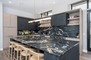 A modern kitchen with a marble island, bar stools, and built-in shelves. - Chateau Cortina-Newly Built 2026, 5 Guest Suites, Ski-In/Out, Ski Lounge, A/C (Mountain Village)