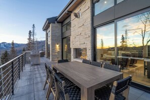 A modern building with a stone facade, large windows, and a patio area with a table and chairs. - Chateau Cortina-Newly Built 2026, 5 Guest Suites, Ski-In/Out, Ski Lounge, A/C (Mountain Village)