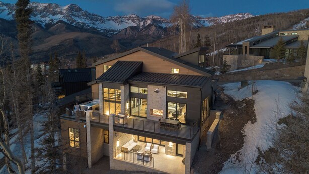 Ein modernes, zweistöckiges Haus mit Kamin, Sitzgelegenheit im Freien und Blick auf verschneite Berge.