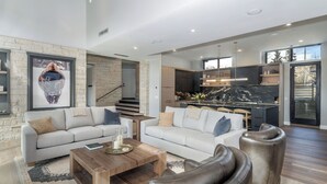 Ein geräumiger Wohnbereich mit Sofa, Couchtisch und Ledersesseln, eine Küche mit Marmorarbeitsplatte und eine Treppe, die eine weitere Ebene hinaufführt.