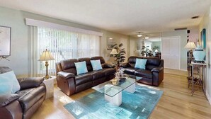 A living room with two leather sofas, a glass coffee table, and a large window with blinds. - Two Family Rooms ! Saltwater Pool ! (Cape Coral)