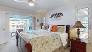 A bedroom with a bed, a ceiling fan, a nightstand, a lamp, and a wall art piece. - Two Family Rooms ! Saltwater Pool ! (Cape Coral)