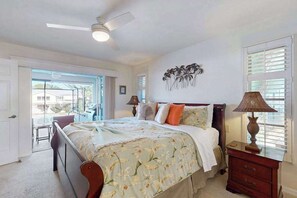 Ein Schlafzimmer mit Bett, Deckenventilator, Nachttisch, Lampe und Wandbild.