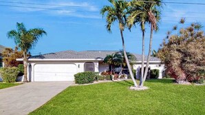 A residential house with a garage, a lawn, and palm trees. - Two Family Rooms ! Saltwater Pool ! (Cape Coral)