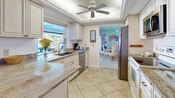 A kitchen with white cabinets, a granite countertop, a ceiling fan, a microwave, and a refrigerator. - Two Family Rooms ! Saltwater Pool ! (Cape Coral)