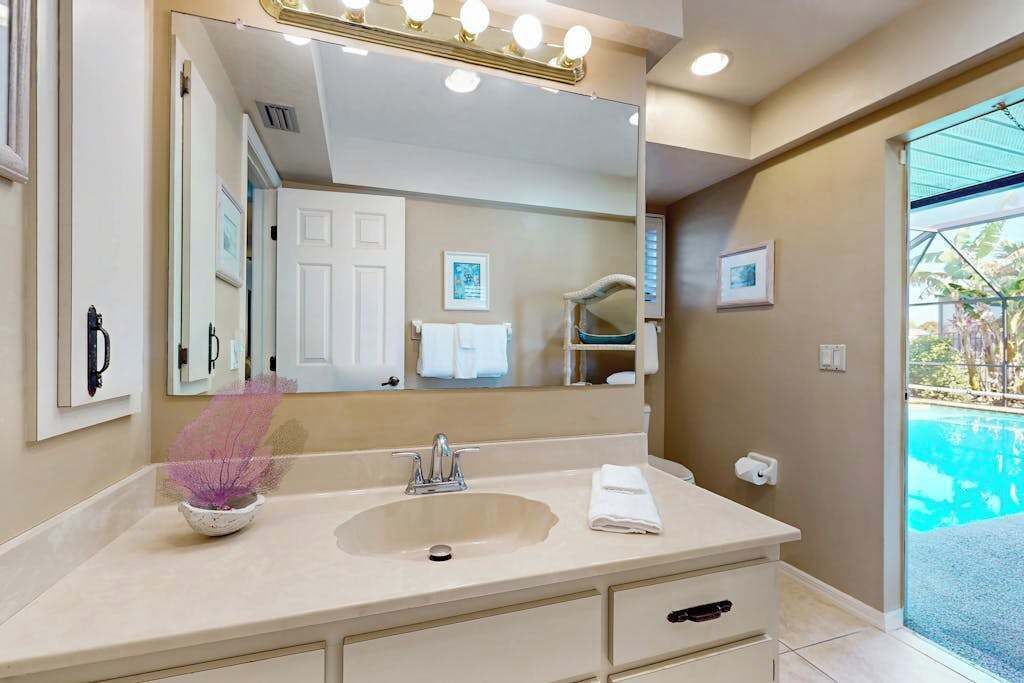 A bathroom with a large mirror, a sink, a towel, and a view of an outdoor pool.