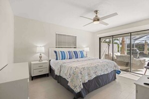 A bedroom with a bed, nightstands, a ceiling fan, a window with blinds, and a view of outdoor furniture. - Dog friendly house with private pool, large dock, and Gulf access (Cape Coral)