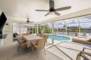 A spacious indoor area with a pool, dining table, chairs, and ceiling fans. - Dog friendly house with private pool, large dock, and Gulf access (Cape Coral)