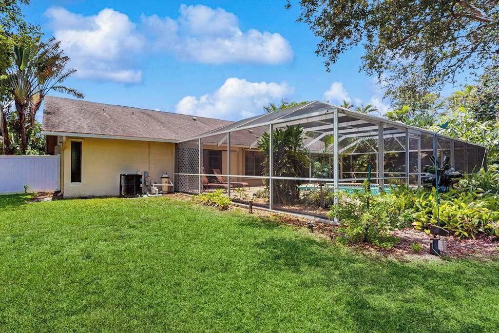 Ein Haus mit überdachter Terrasse, Rasenfläche und verschiedenen Pflanzen.