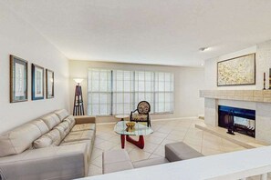 A living room with a sofa, a round coffee table, a fireplace, and large windows with blinds. - Spacious home with heated pool, WiFi, washer & dryer, and lanai (Fort Myers)